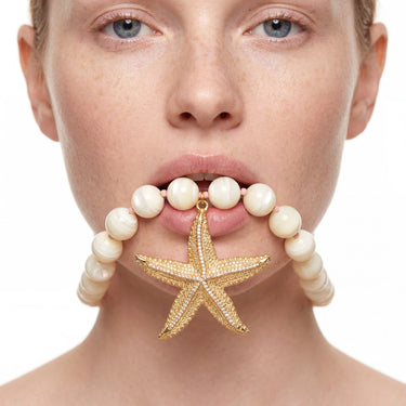 Pearl bead necklace with gold starfish pendant held in model's mouth, close-up studio shot