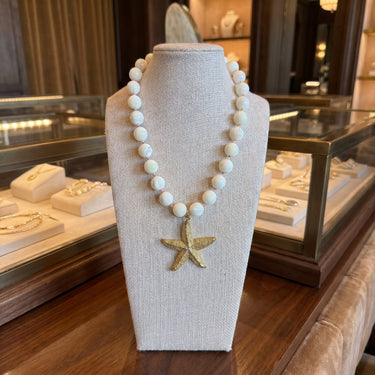 White beaded necklace with a gold starfish pendant displayed on a linen bust in a jewelry store