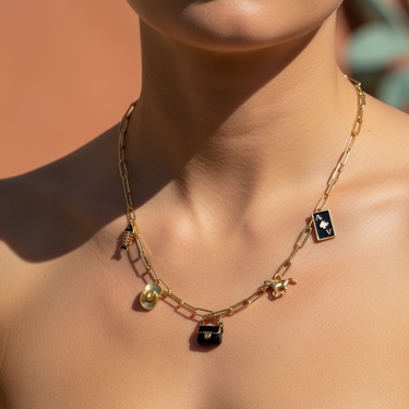 Close-up of black enamel bag charm on stacked gold charm bracelet