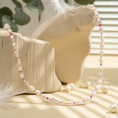 Pearl necklace with colorful beads on a wooden surface with feathers and leaves.