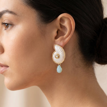 Nautilus shell drop earrings in white and gold with a pale blue stone, worn on a model