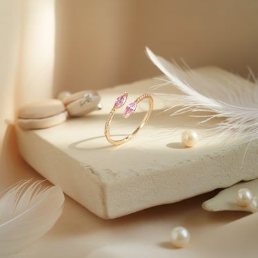 Gold Sunrise Horizon Kiss Ring with pink gemstones on a stone surface with feathers