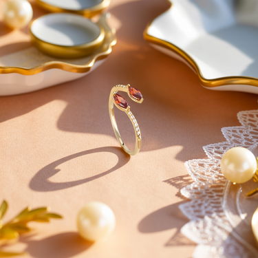 Gold Sunset Horizon Kiss Ring with red gemstones on a decorative surface with pearls and lace