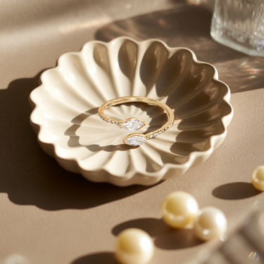 Gold Horizon Kiss Ring with a diamond on a decorative ceramic dish with pearls around.