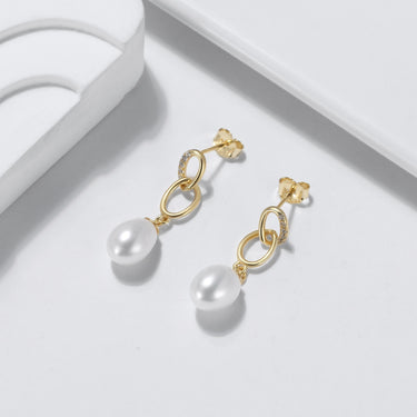 Close-up of pearl and CZ gold drop earrings on white ceramic.