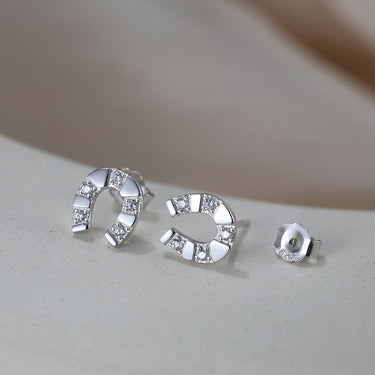 Close-up of silver horseshoe earrings with 5A CZ stones on curved ceramic surface.
