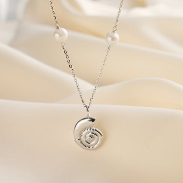 Silver nautilus pendant necklace with pearls on soft fabric.