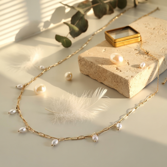 Pearl raindrop necklace with pearls on a light surface with a feather and leaves.