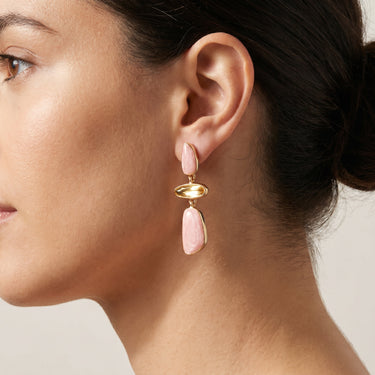 Drop earrings with pink stone pieces and a gold oval connector, worn on a model