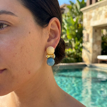 Double sphere earrings with cream and aqua beads and gold connector, worn outdoors near a pool