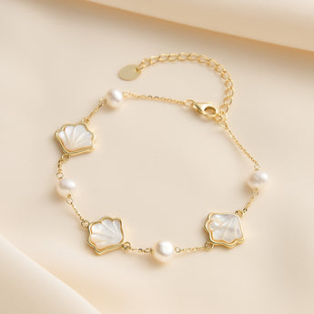 Gold plated bracelet with pearl and shell charms on neutral background.