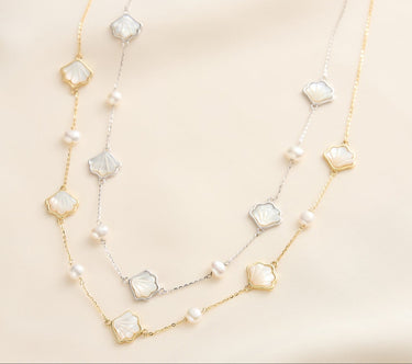 Gold and silver seashell and pearl necklace on beige surface.