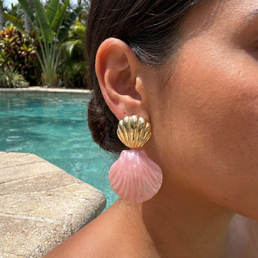 Shell drop earrings in gold brass and pink worn on a model outdoors by a pool