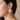 Gold-tone sunburst stud earrings with a white baroque pearl center, worn on a model