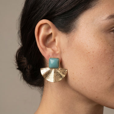Gold brass fan shaped statement earring with turquoise stone worn on a model's ear